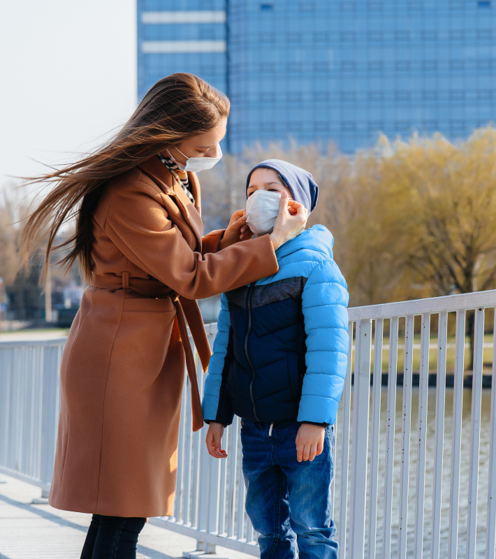 Mamá poniendole a su hijo la mascarilla en un parque.